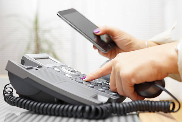 Woman is dialing on land line phone and looking on mobile phone Woman is dialing on land line phone and looking on mobile phone